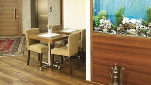 A room with a wooden floor, a dining table with chairs, a large aquarium, and a traditional metal lamp.