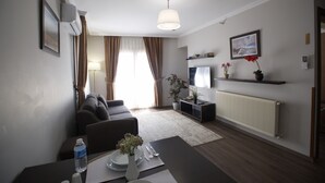 A modern living room with a sofa, a dining table with a vase of flowers, a TV, and a radiator.