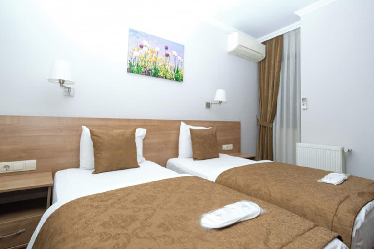 A hotel room with two beds, a painting on the wall, and an air conditioning unit.