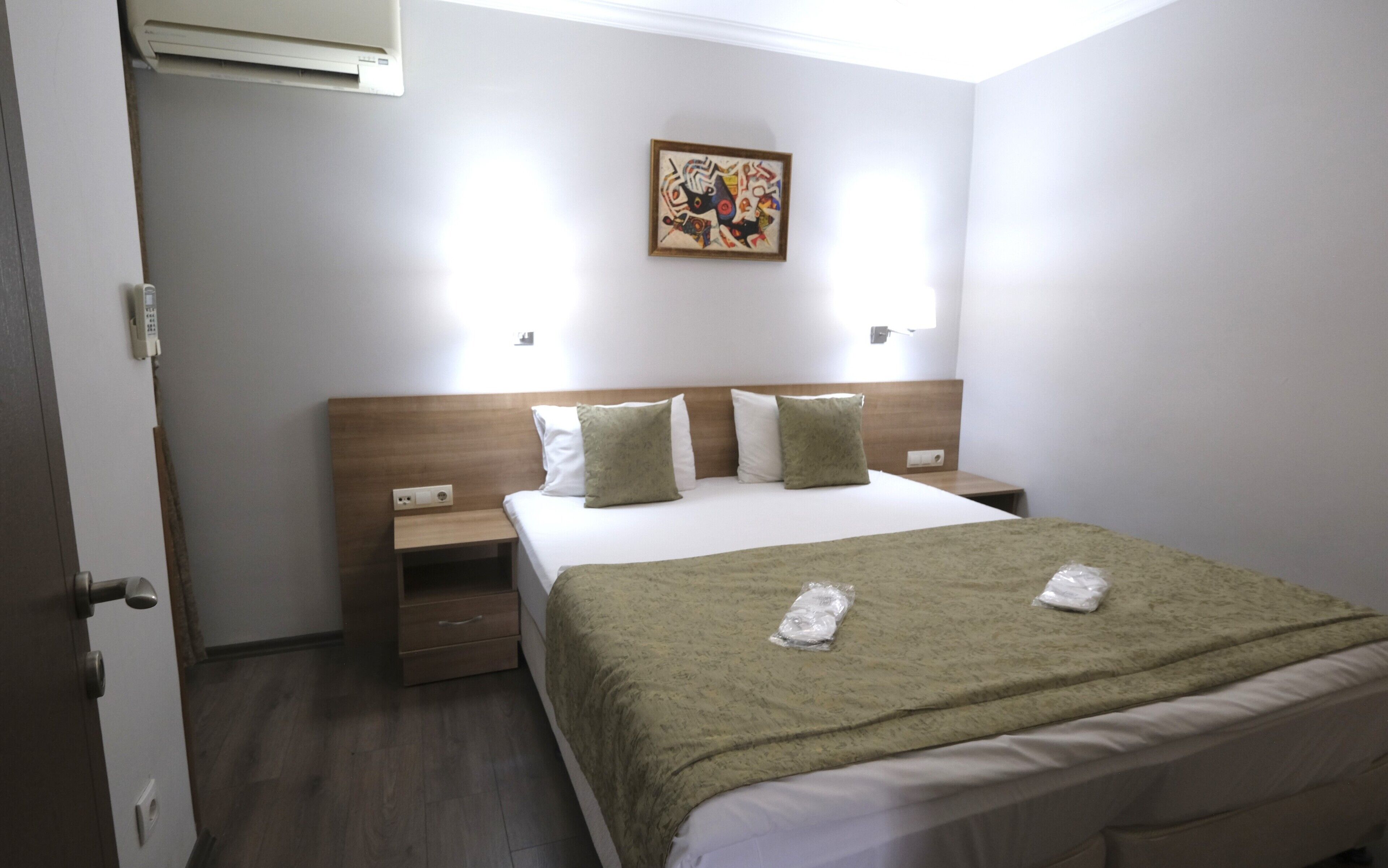 Quarto de hotel com cama, mesas de cabeceira, ar condicionado fixado na parede e um quadro na parede.