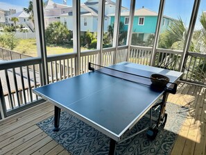 A ping pong table on a wooden deck with a view of houses and palm trees.