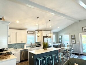 A spacious kitchen with white cabinets, a central island with stools, and pendant lighting.