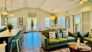 A spacious living room with a green sofa, a wooden coffee table, and a dining area with a long table and chairs. - Steps away from Grayton Beach, Large Private Saltwater Pool, 4 Bedrooms, 4 Baths (Santa Rosa Beach)