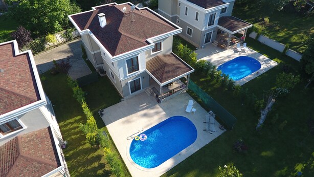 Una casa de dos pisos con un patio trasero grande, piscina y un área de patio techada.