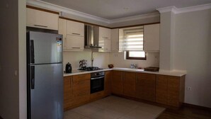 Una cocina moderna con un refrigerador de acero inoxidable, armarios de madera, una estufa a gas y una ventana con persianas.