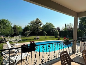 A poolside area with a clear view of a swimming pool, surrounded by a metal railing, and featuring outdoor seating and a hammock.