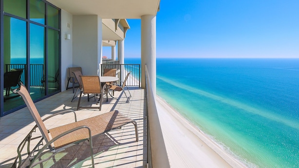 A balcony with a view of the ocean, a table with chairs, and a window with blinds. - The Oasis at Orange Beach, formerly known as Phoenix West II, Unit 2308 (Orange Beach)