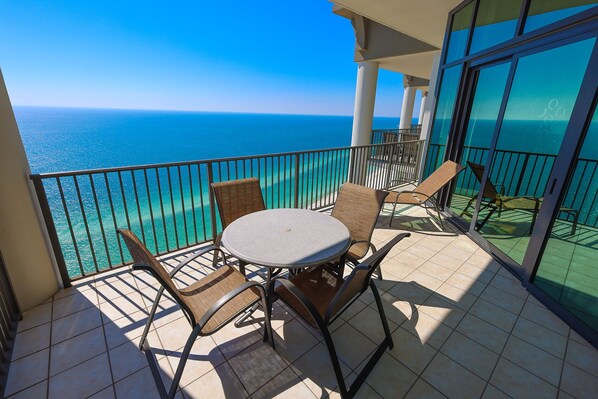 Un balcon avec une table ronde et des chaises, donnant sur une mer d’un bleu limpide.