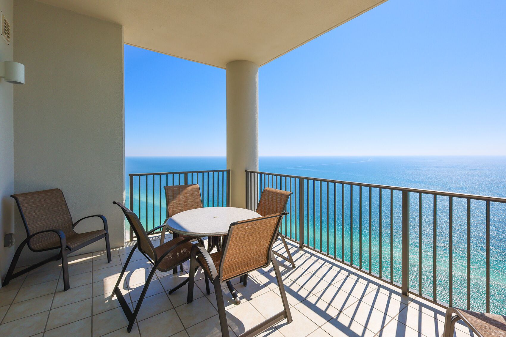 A balcony with a round table and four chairs, overlooking a clear blue sea.