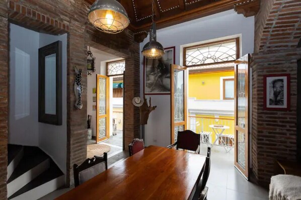 Un comedor con una mesa y sillas de madera, una lámpara colgante y vistas a un balcón con mobiliario exterior.