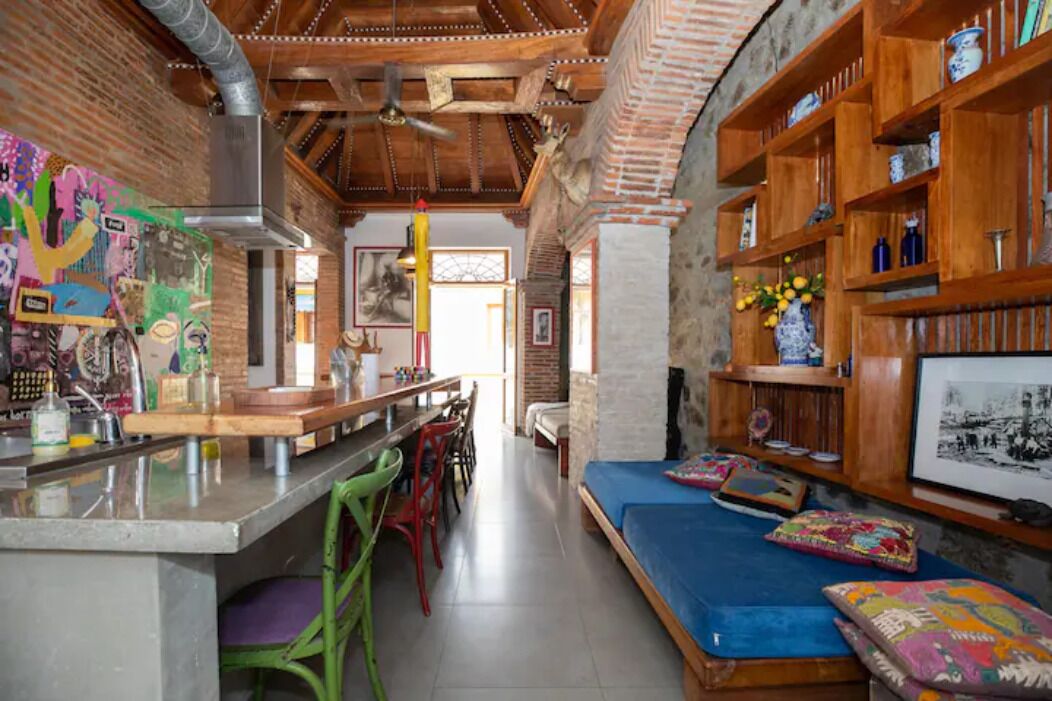 A cozy interior with a kitchen area, a dining space, and a seating area with cushions.