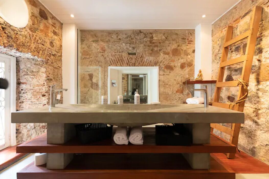 A bathroom with a large stone wall, a modern sink, and a wooden bench.