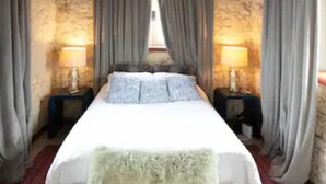 A bedroom with a large bed, wooden beams on the ceiling, and two bedside tables with lamps.