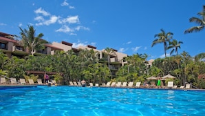Una piscina con sillas de descanso y palmeras, rodeada de edificios de hotel.