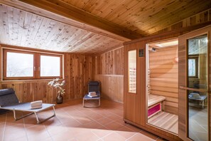 A wooden cabin with a sauna, a massage table, and a window with a view of the snowy landscape. - Familienparadies MoNi (Thiersee)