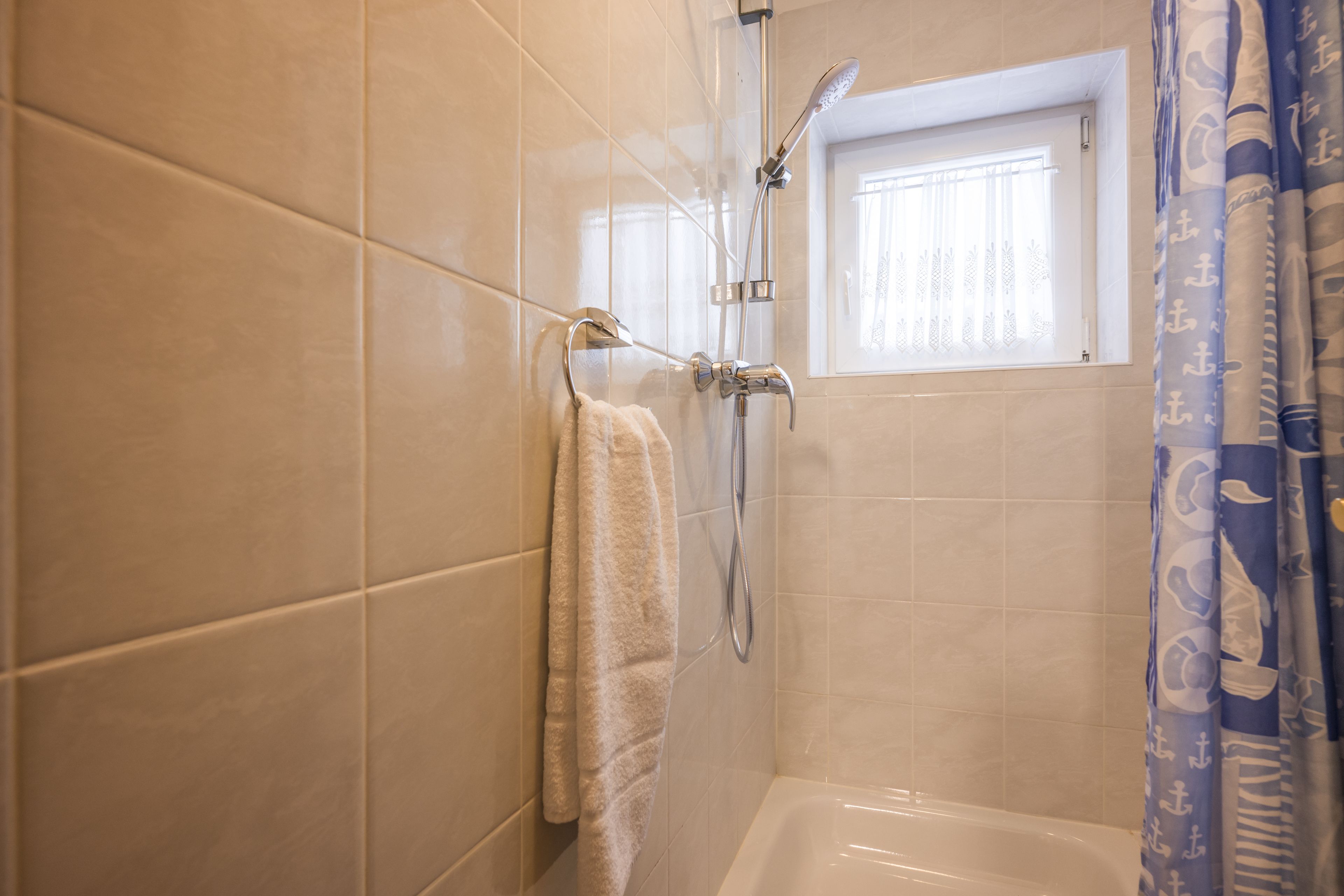 A bathroom with a bathtub, a shower, and a window with a curtain.