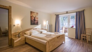 Een slaapkamer met een houten bed, nachtkastjes, gordijnen voor het raam en uitzicht op groen.