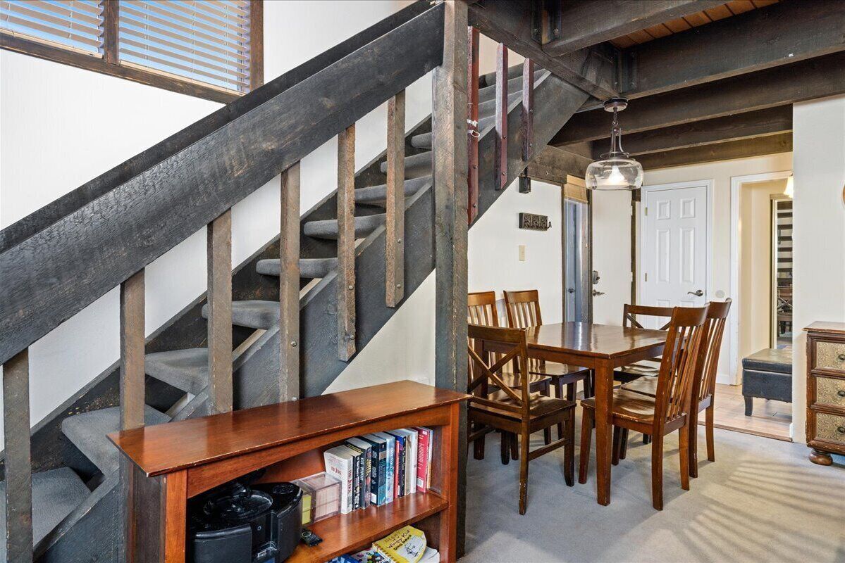 A staircase with a wooden handrail and a dining area with a table and chairs.