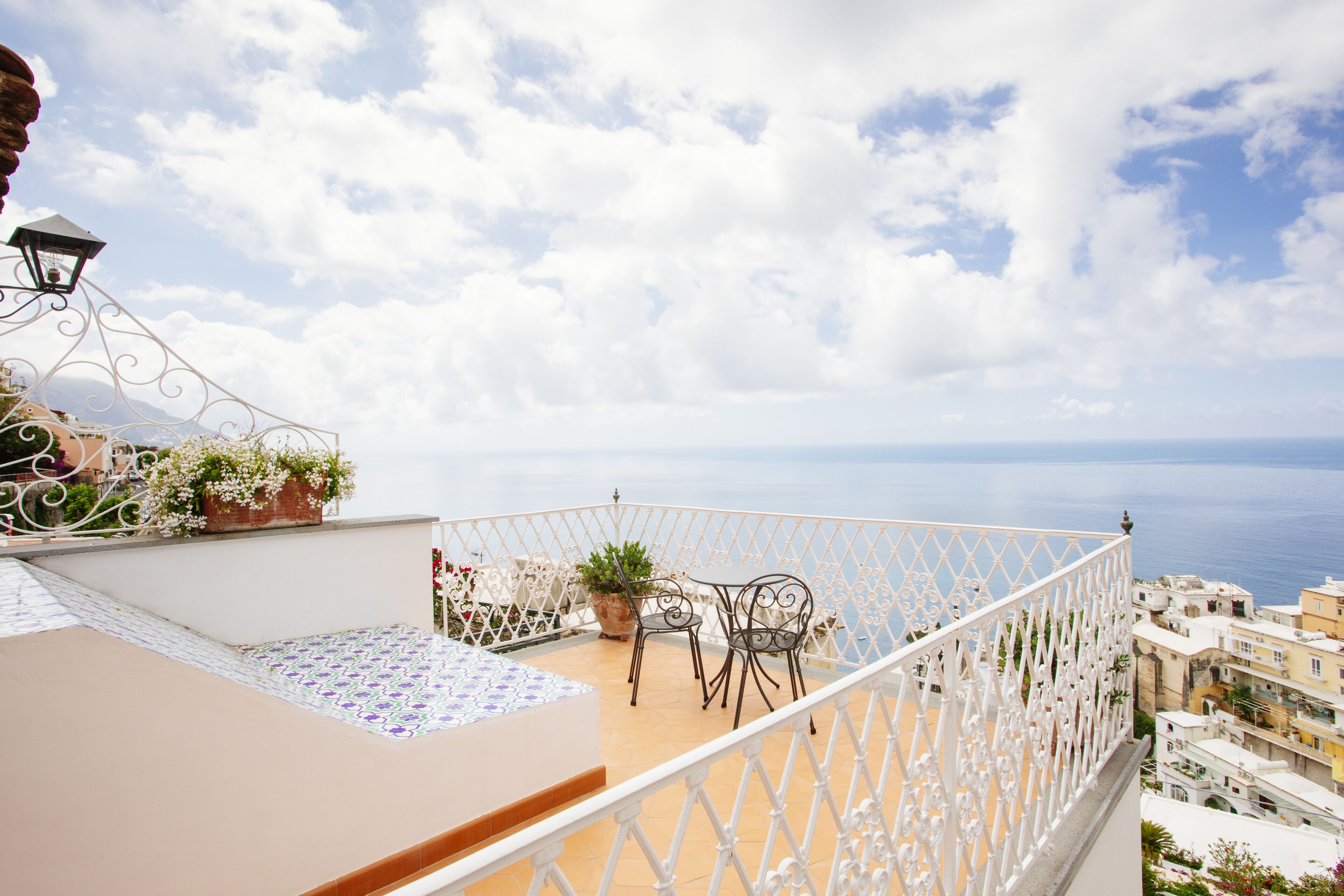 A balcony with a white railing, a potted plant, and two chairs.