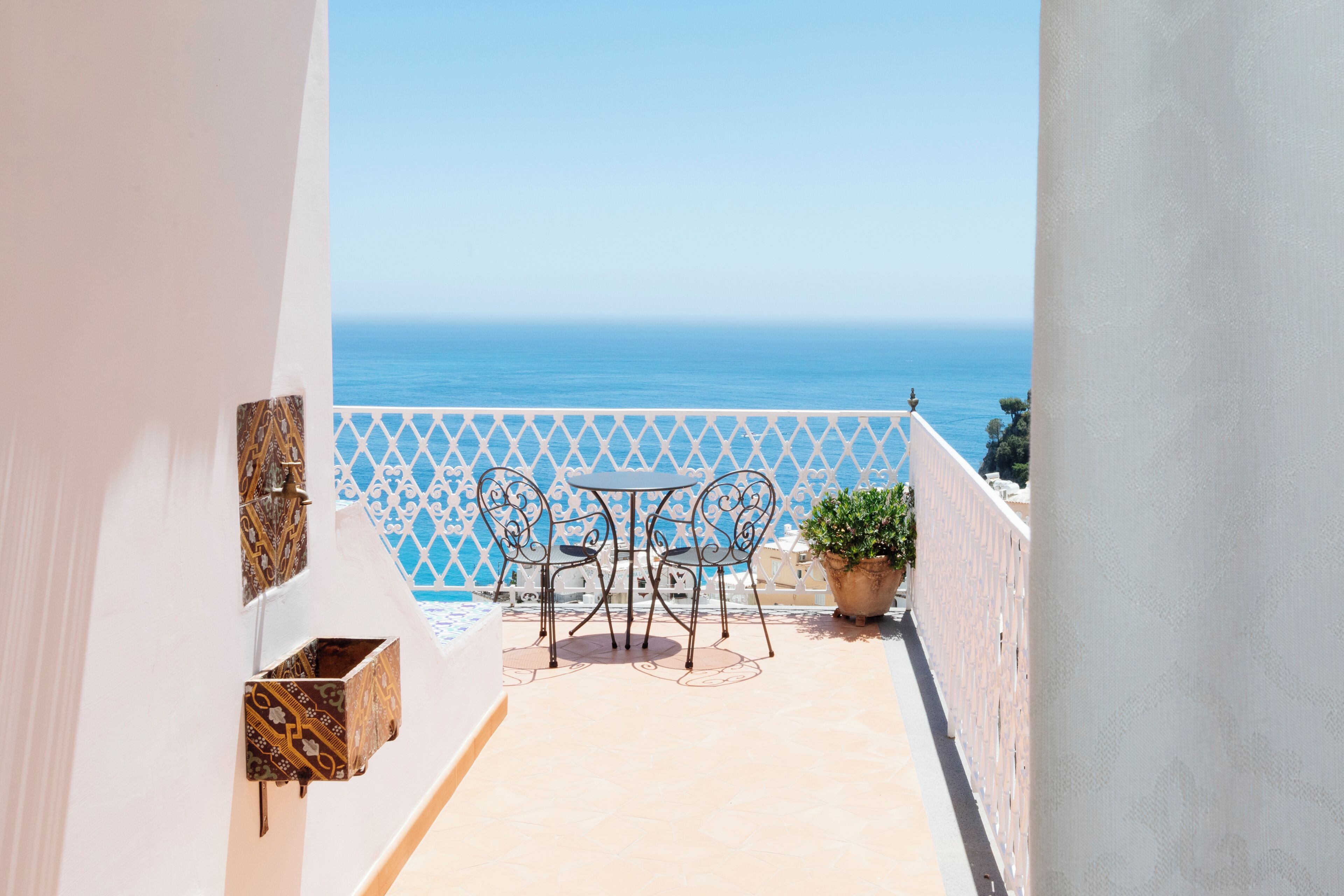 A balcony with a view of the sea, a table with chairs, and a potted plant.