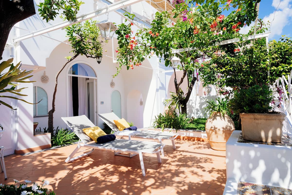 A sunlit outdoor seating area with lounge chairs and potted plants.