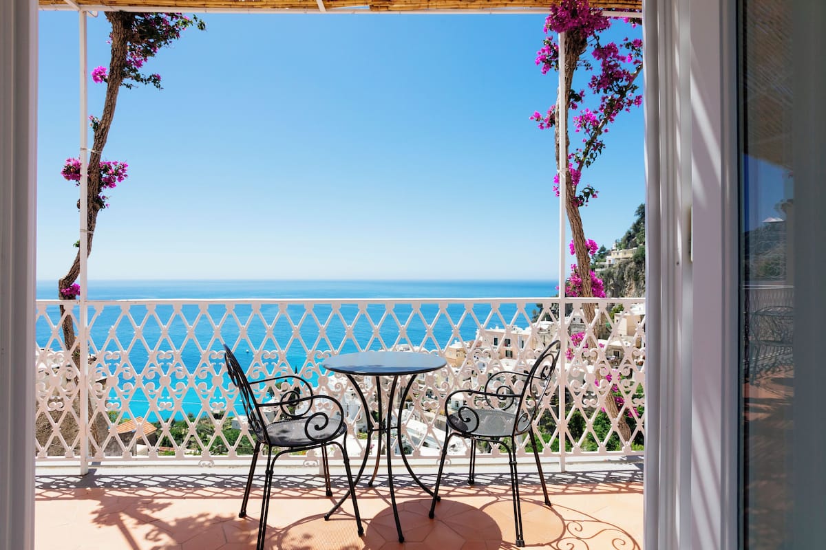 A balcony with two chairs and a table, overlooking a coastal view.