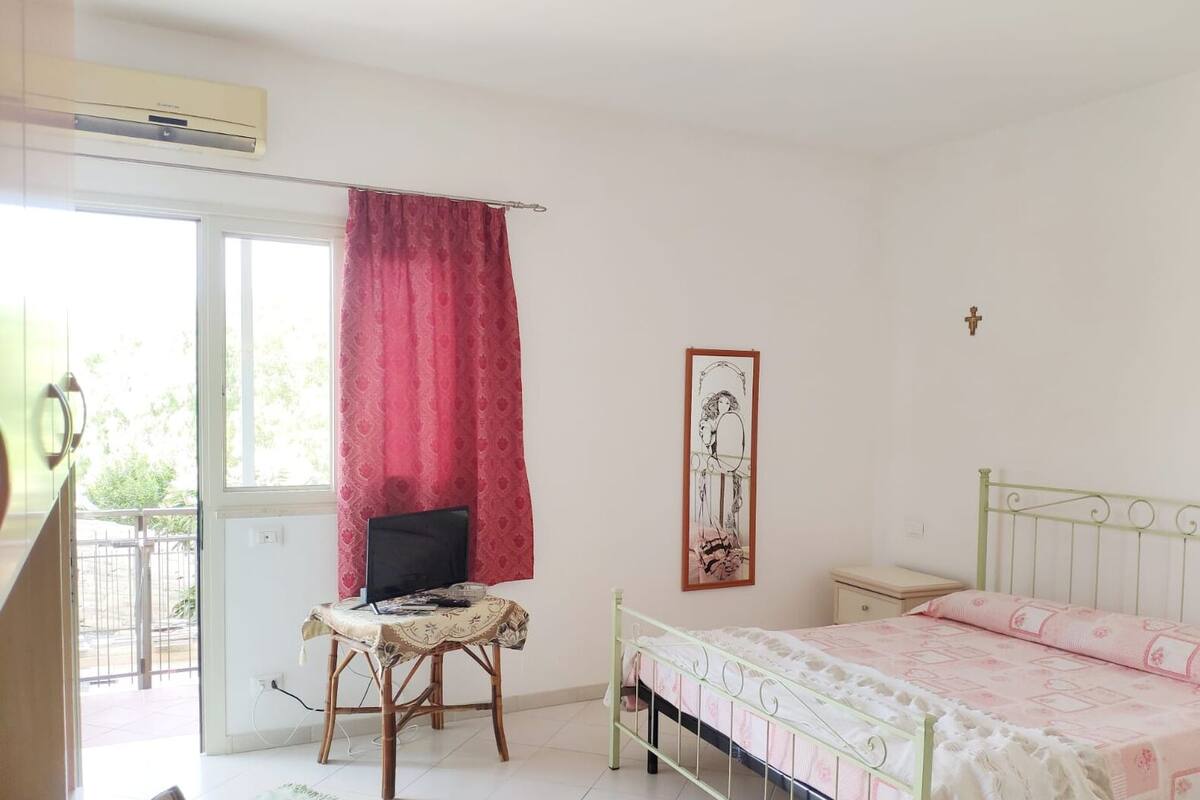 Un dormitorio con cama, un escritorio con silla, una ventana con cortina y un cuadro colgado en la pared.