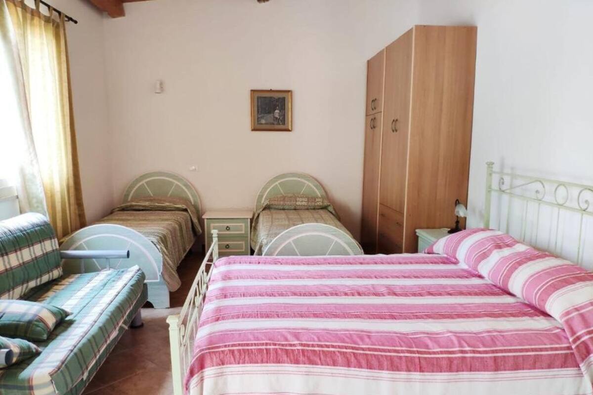 Un dormitorio con dos camas individuales, un armario de madera, un sillón verde y una mesita.
