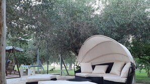 Un área de estar al aire libre con un banco acolchado y un sofá cubierto, rodeado de árboles.
