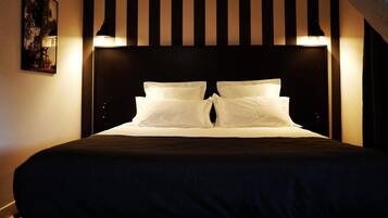 A neatly made bed with white linens and a dark headboard, illuminated by wall-mounted lights.