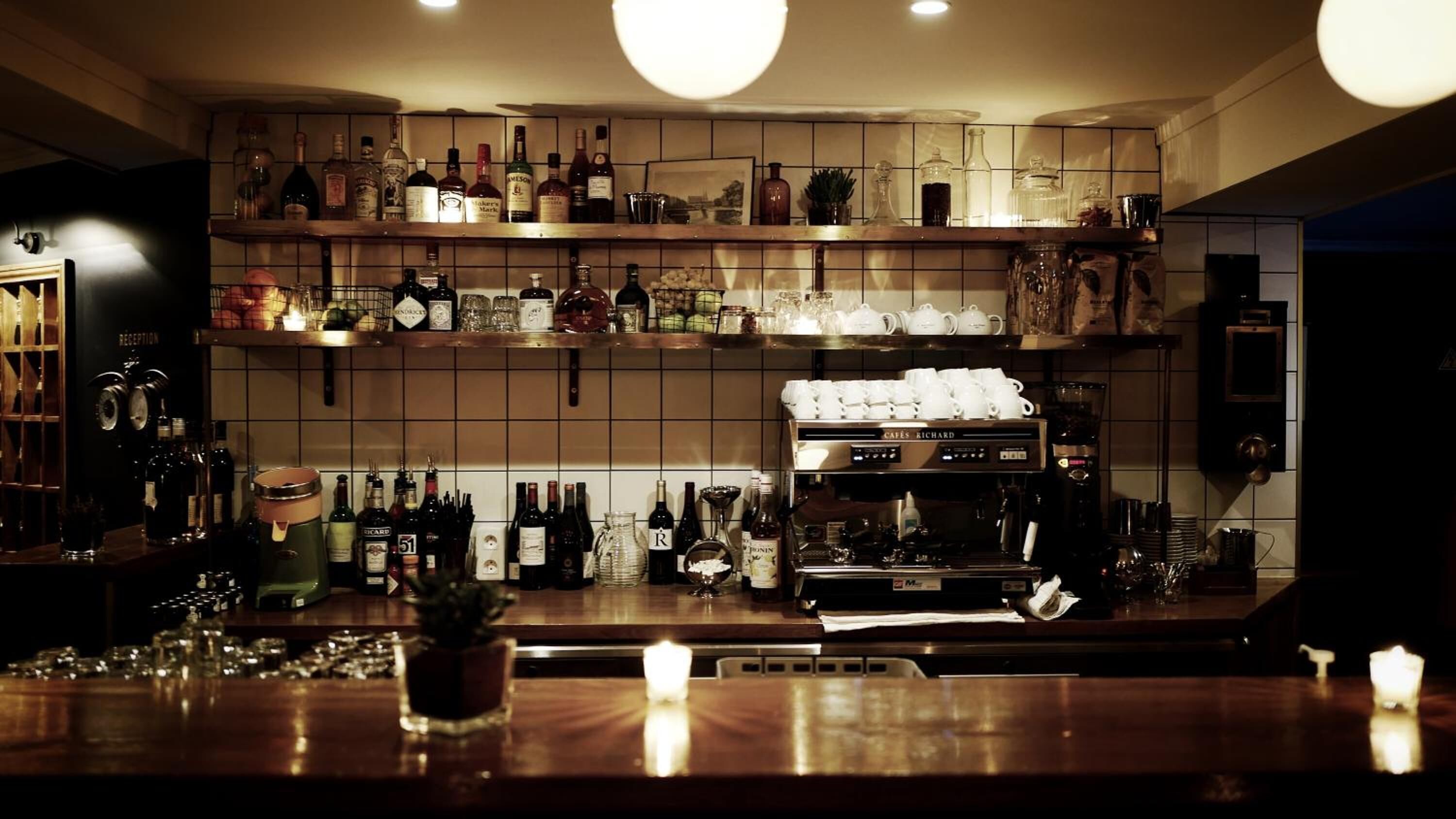 Zona de bar con estanterías llenas de botellas y vasos, una máquina de café y una recepción.