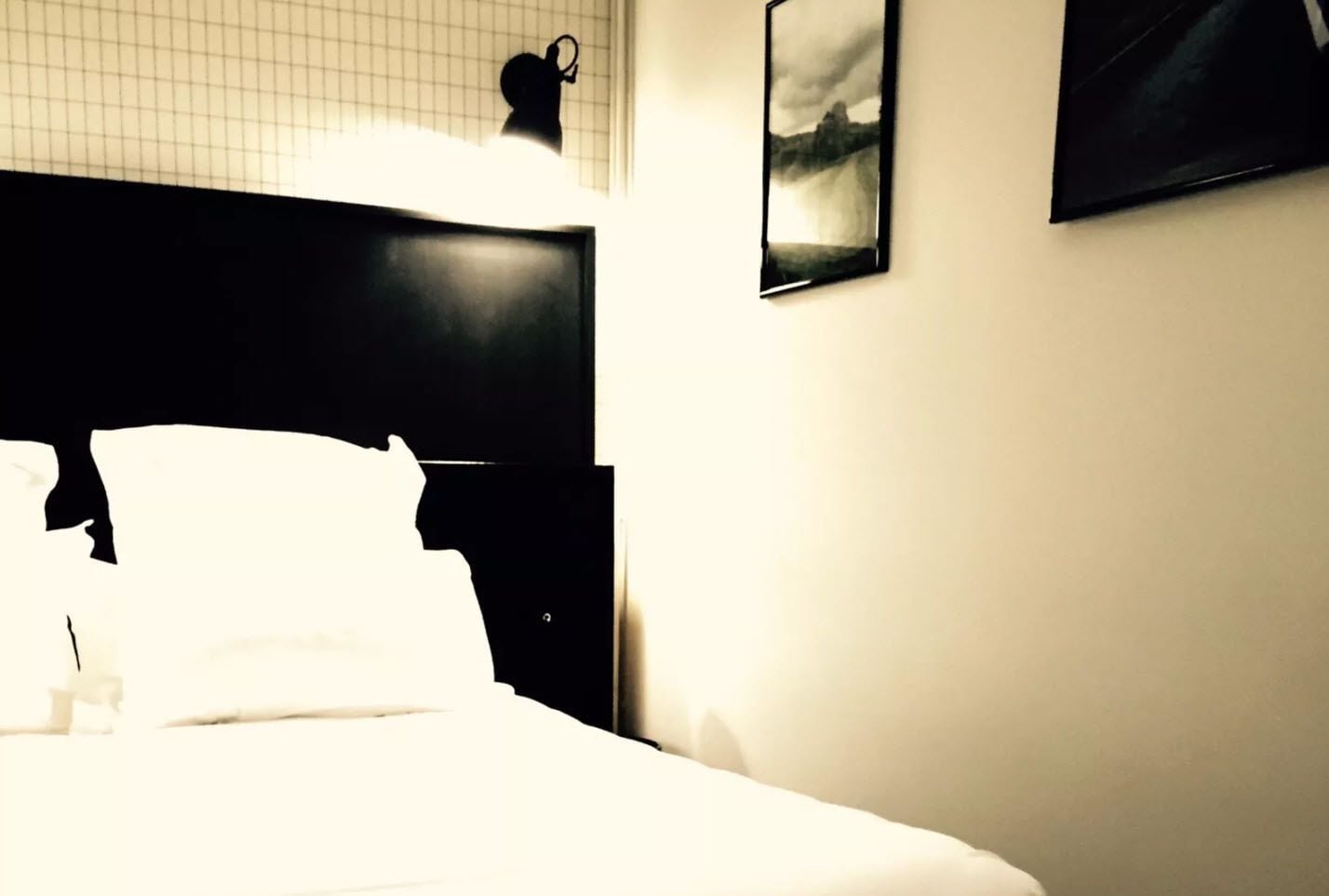 Une chambre d’hôtel avec un lit, une table de chevet, une lampe fixée au mur et un tableau encadré.