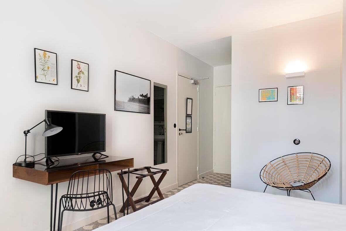 A bedroom with a bed, a desk with a computer, a chair, and a wall-mounted lamp.