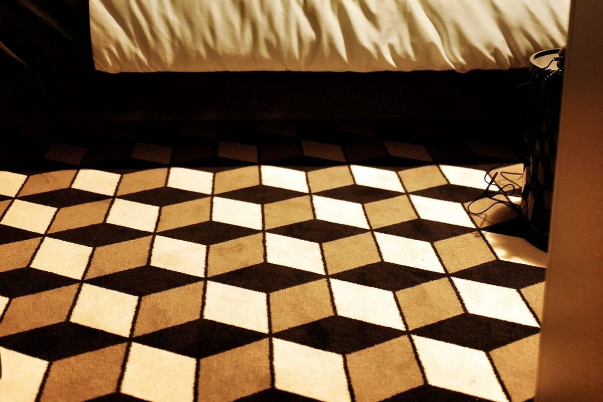 Une chambre d’hôtel avec un lit, une tête de lit, une lampe fixée au mur et un sol à motifs.