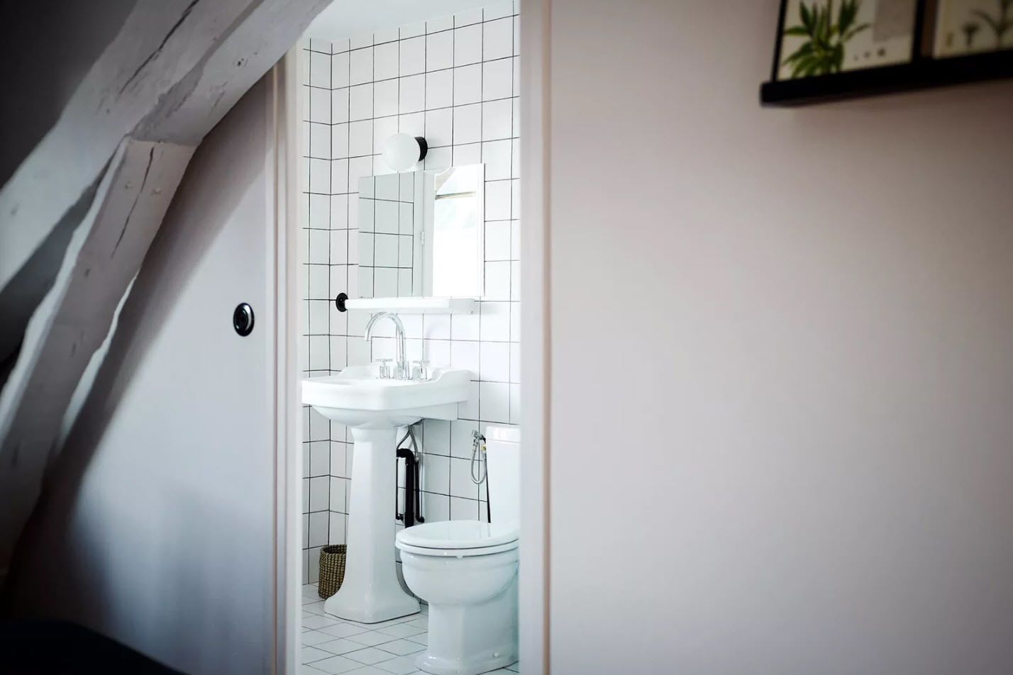 Un baño con lavamanos pedestal blanco, inodoro y espejo sobre el lavamanos.