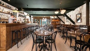 Un restaurante con barra y mesas de madera, sillas negras y una pared de piedra.
