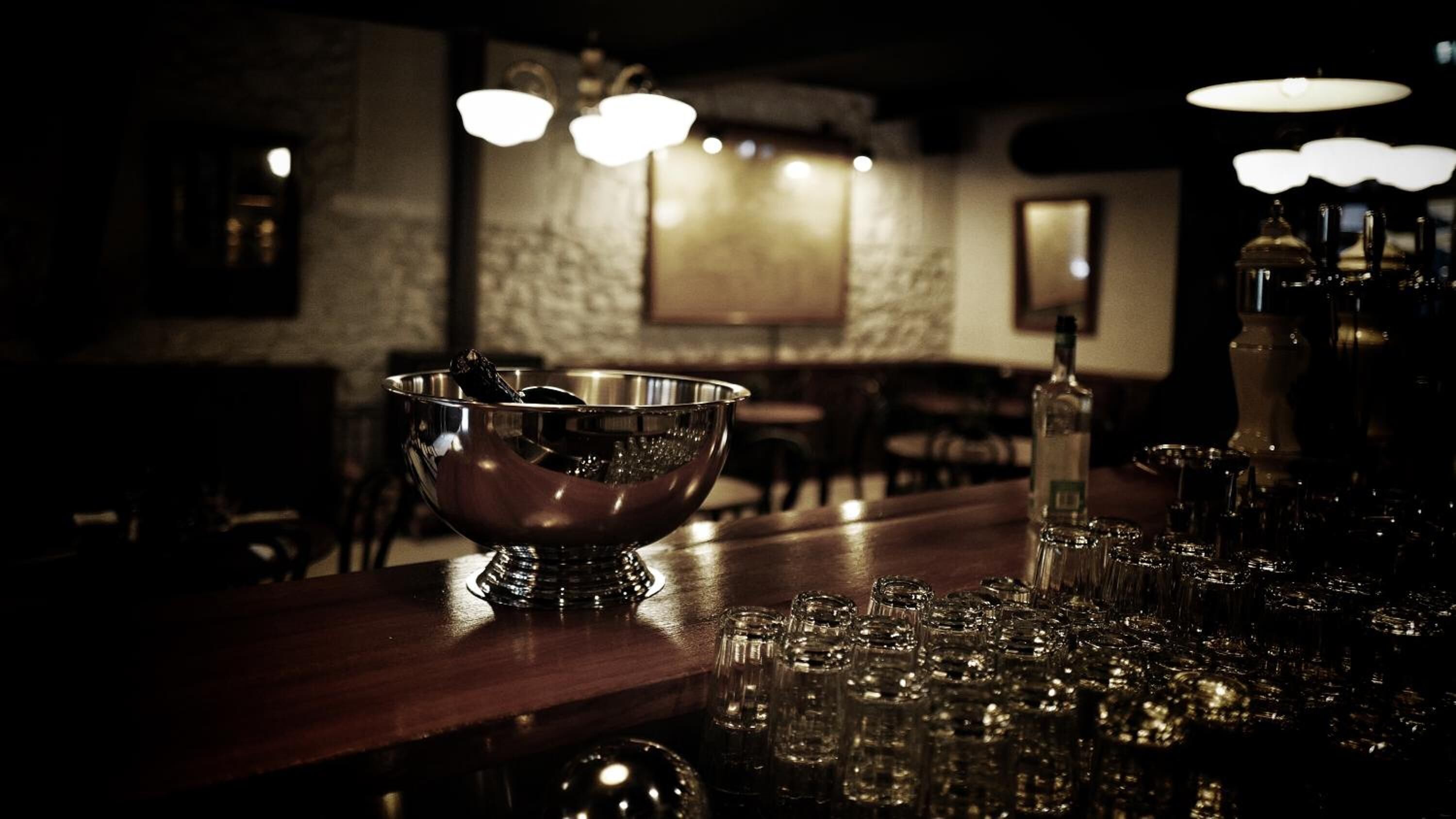 A bar area with a metal bowl, glasses, and bottles on the counter.