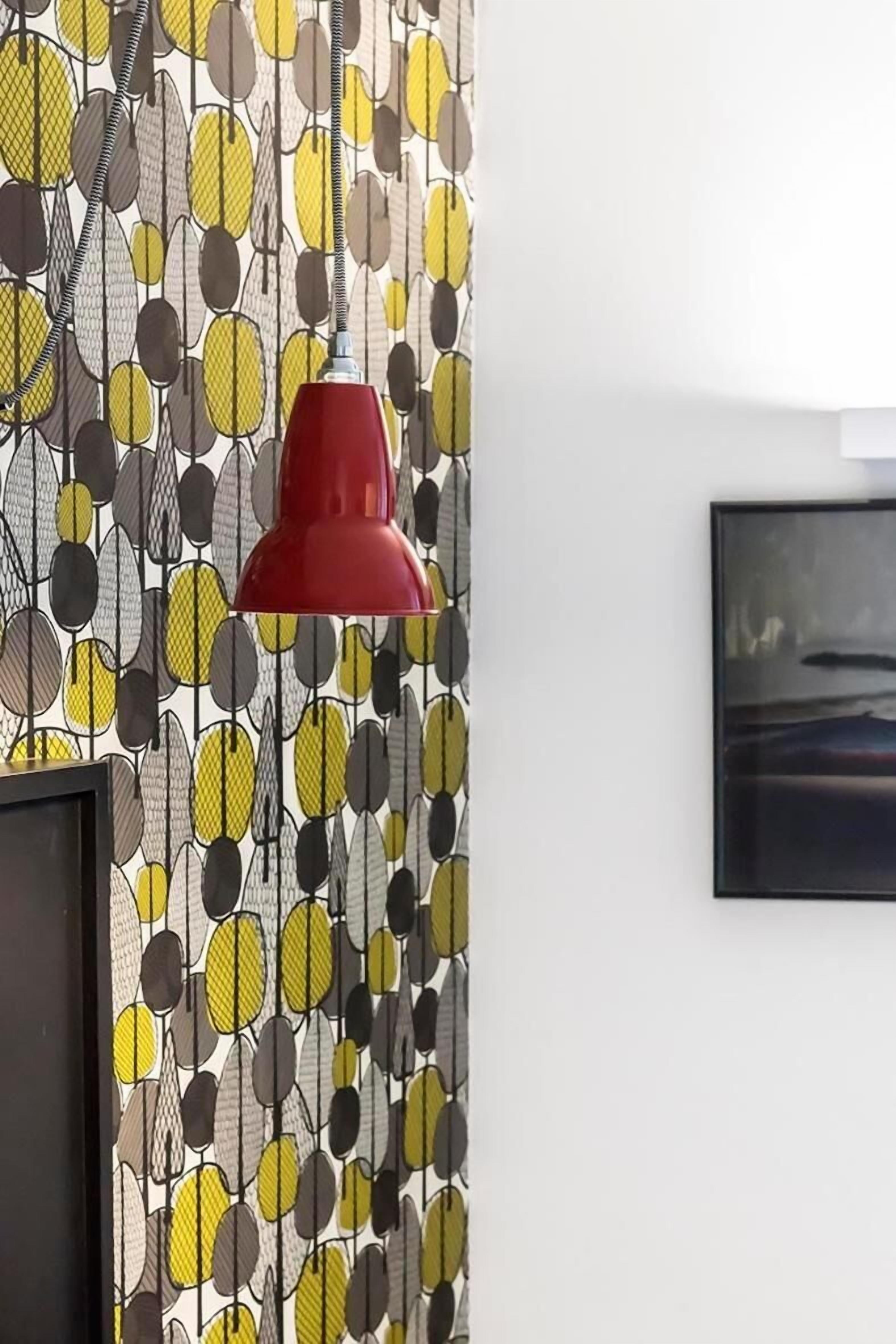 Una habitación con papel tapiz estampado, una lámpara colgante roja y un cuadro en la pared.