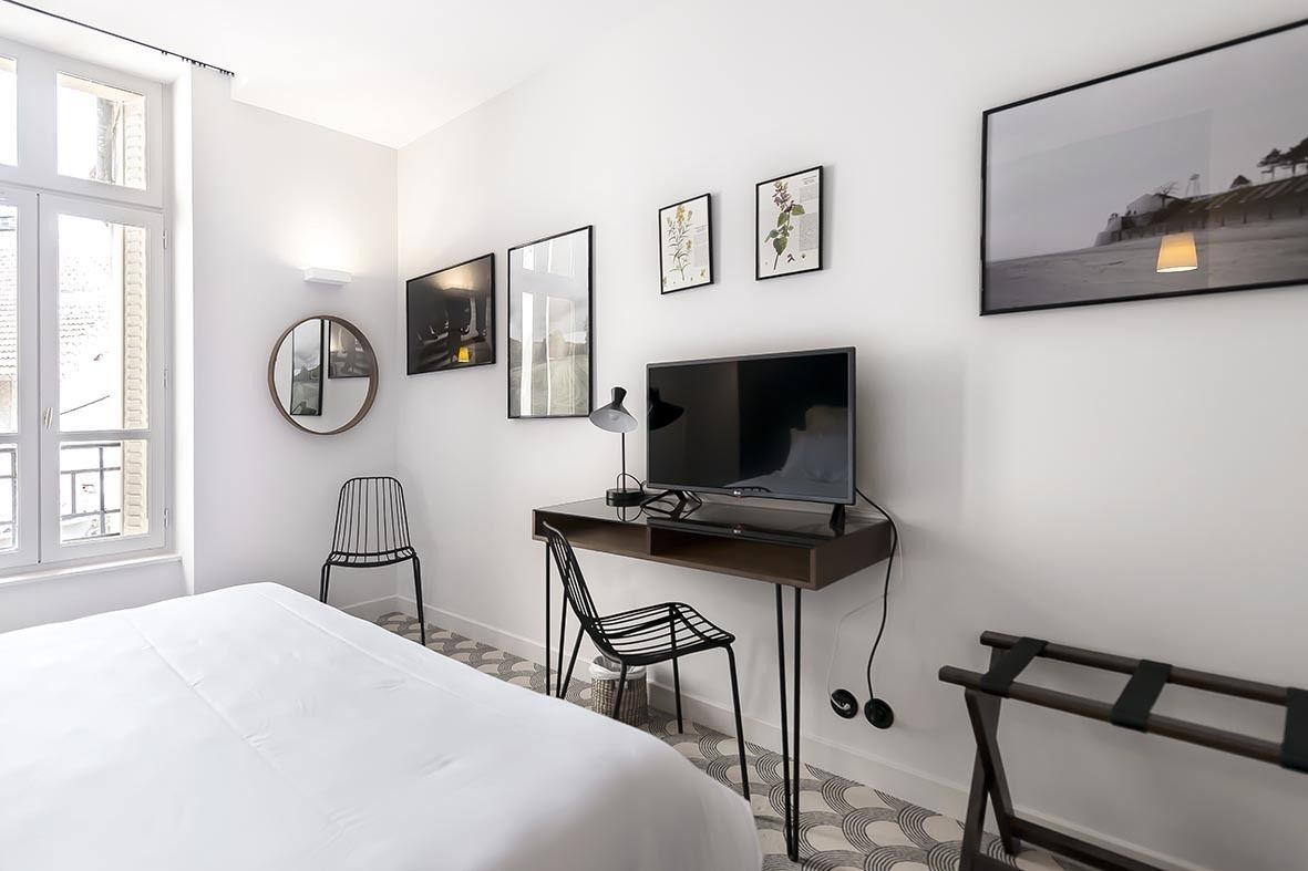 A hotel room with a bed, a desk with a TV, a chair, and framed pictures on the wall.