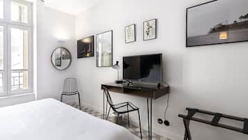 A hotel room with a bed, a desk with a TV, a chair, and framed pictures on the wall.