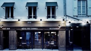 Un edificio con tres entradas identificadas como "CAFÉ BAR", "HÔTEL DES CARMES" y "RESTAURANT".