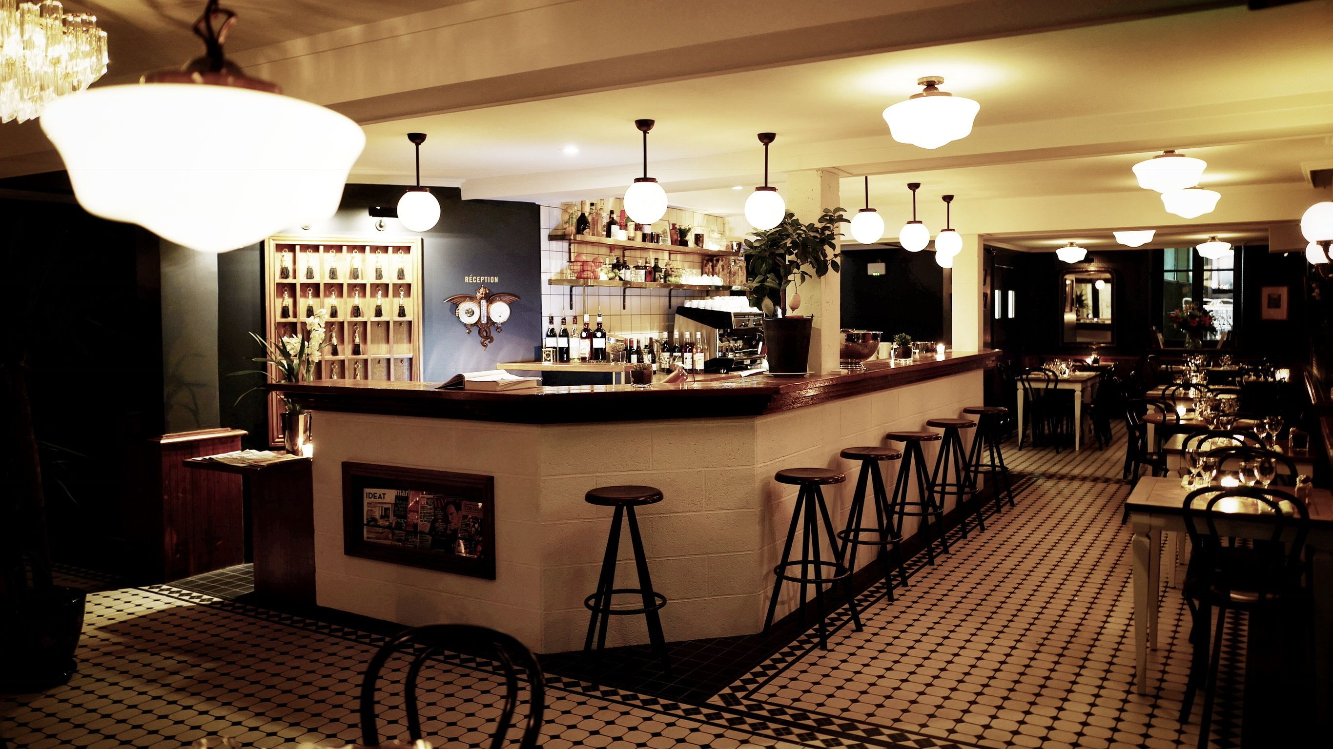 A bar area with a reception desk, bar stools, and a variety of bottles and glasses on shelves.