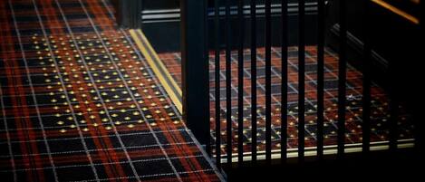 Una escalera con barandilla negra y alfombra roja y negra a cuadros.