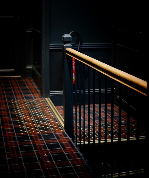 A staircase with a black railing and a red and black checkered carpet. - Hôtel des Carmes (Aurillac)
