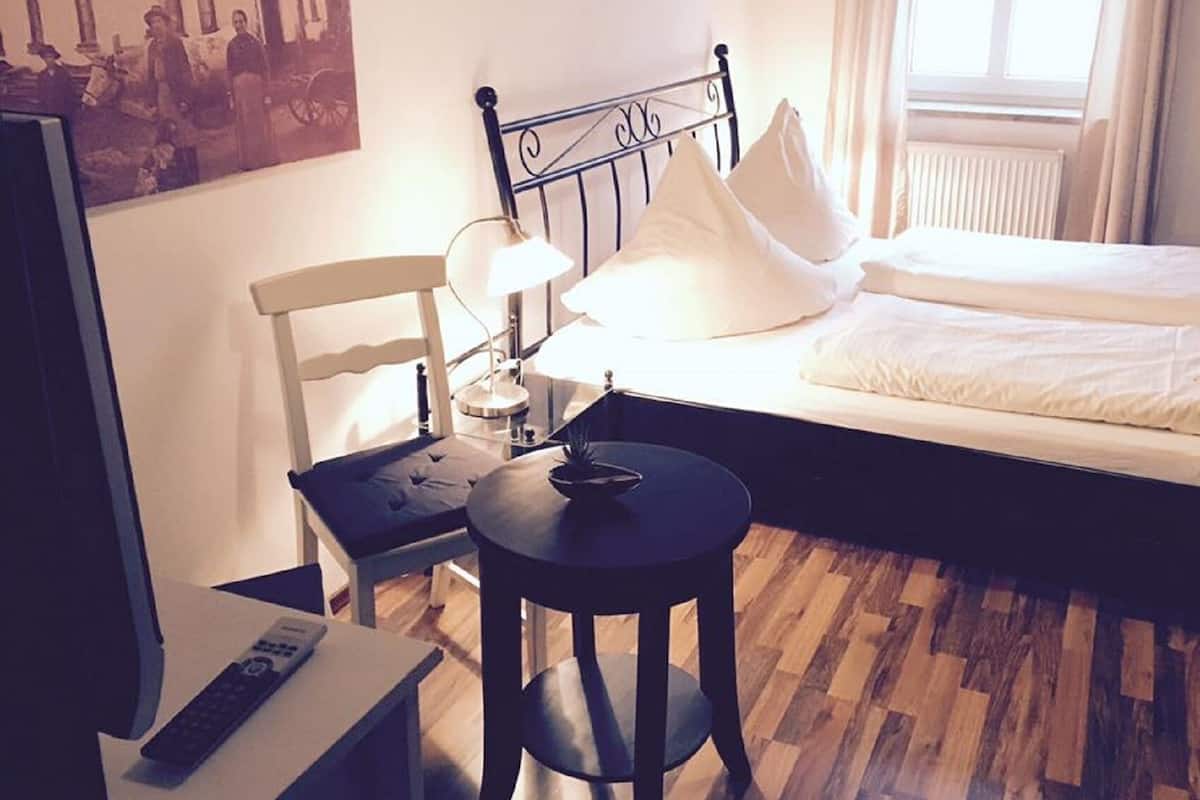 Ett hotellrum med en säng, en stol, ett litet bord, en lampa och en tv.