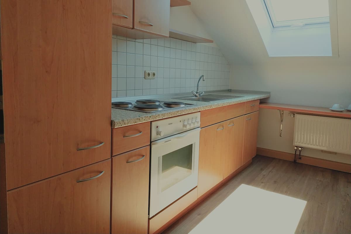 Ett kök med träskåp, vita kakelplattor ovanför arbetsbänken, en inbyggd ugn och ett fönster ovanför diskhon.
