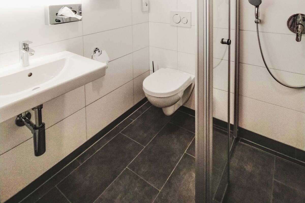 Ett modernt badrum med en dusch som är avskärmad med glasväggar, ett vitt handfat och en toalett.