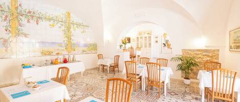 A restaurant with white tables and chairs, a large painting on the wall, and a patterned floor.