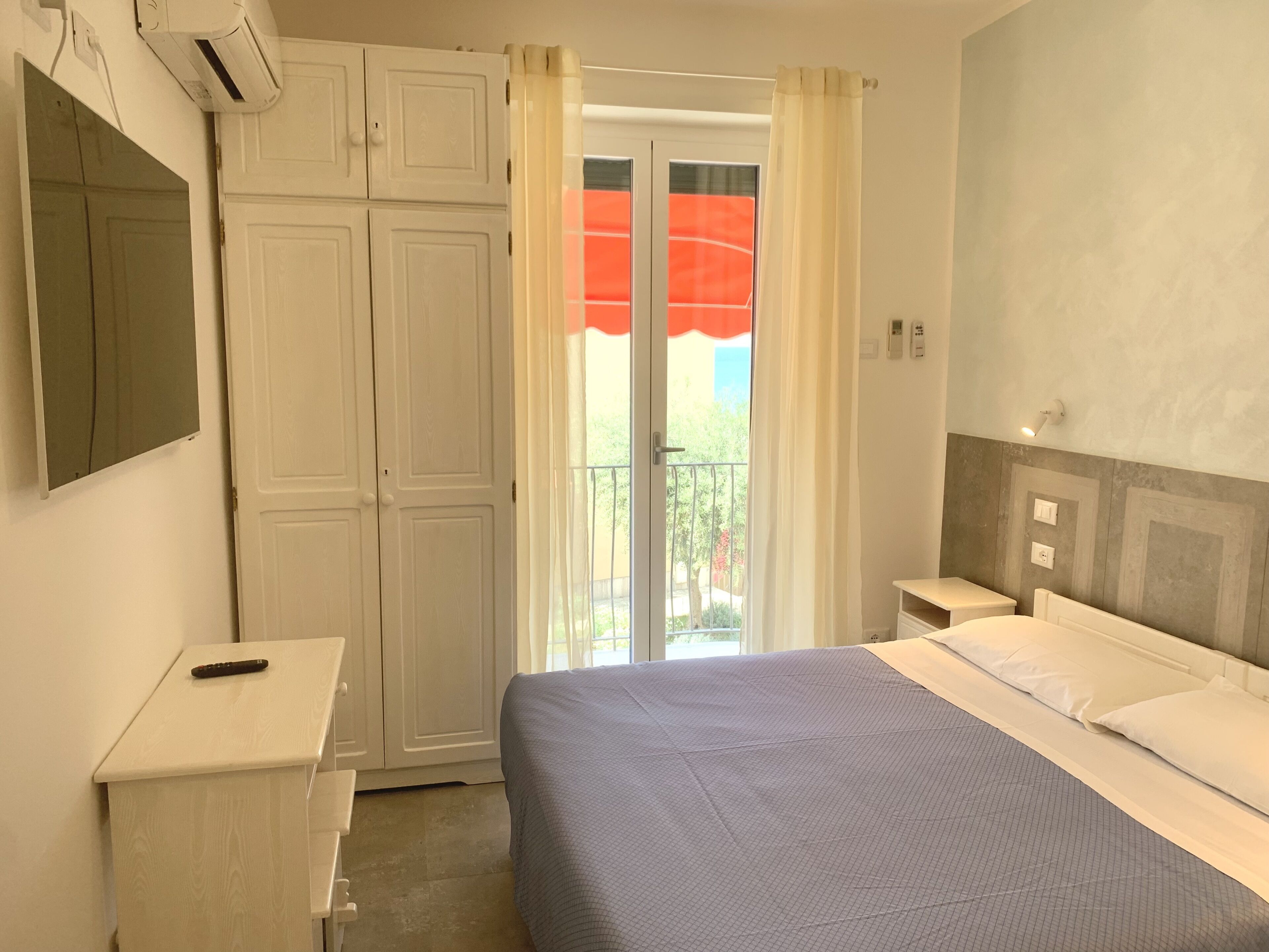 A bedroom with a bed, a desk, a wardrobe, and a balcony with a view.