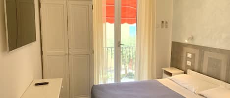 A bedroom with a bed, a desk, a wardrobe, and a balcony with a view.